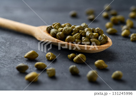 Marinated capers in a wooden spoon on a black marble background, selective focus. Marinated capers in a wooden spoon on a black marble background, selective focus. 131245996