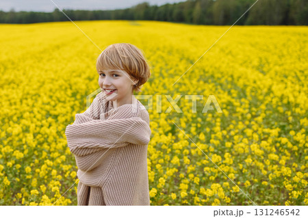 Smiling girl in oversized beige sweater hugging herself in yellow flower field Smiling girl in oversized beige sweater hugging herself in yellow flower field 131246542