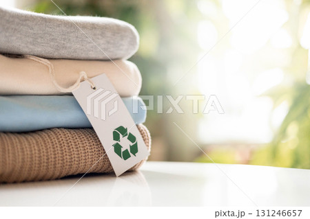 Stack of folded sustainable clothes with recycling tag on white table, eco-friendly concept 131246657
