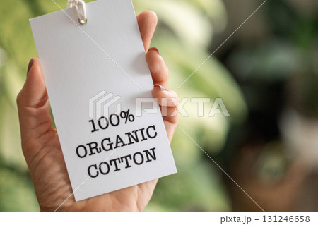 Hand Holding Organic Cotton Label on Eco-Friendly Background with Soft Natural Light Hand Holding Organic Cotton Label on Eco-Friendly Background with Soft Natural Light 131246658