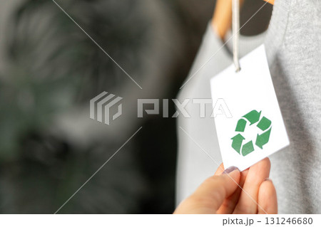 Hand holding eco-friendly tag with recycle symbol on gray sustainable clothing in soft focus Hand holding eco-friendly tag with recycle symbol on gray sustainable clothing in soft focus 131246680