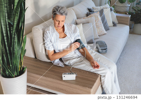 Senior woman checks blood pressure at home with digital monitor, daily health care routine Senior woman checks blood pressure at home with digital monitor, daily health care routine 131246694