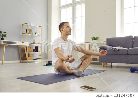 Attractive man in sports outfit doing yoga and meditating on exercise mat Attractive man in sports outfit doing yoga and meditating on exercise mat 131247507