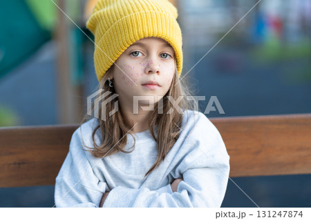 Serious girl in cap sitting arms crossed on bench Serious girl in cap sitting arms crossed on bench 131247874