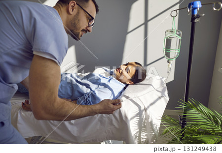 Sick young female patient lying on the couch in hospital receiving IV drip infusion. 131249438