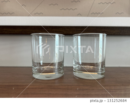 Two clean empty clear glass tumblers on a smooth textured wooden table surface 131252684