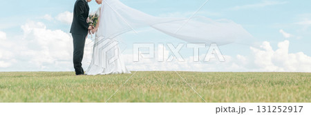 ベールをなびかせる空バックの新郎新婦（ウェディング・結婚式・ブライダル・フォトウェディング） 131252917