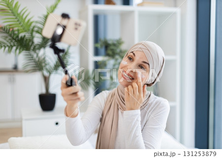 Young Muslim woman in her 20s recording skincare video applying facial cream indoor setting. Promotes self-care, beauty, and digital content creation. 131253879