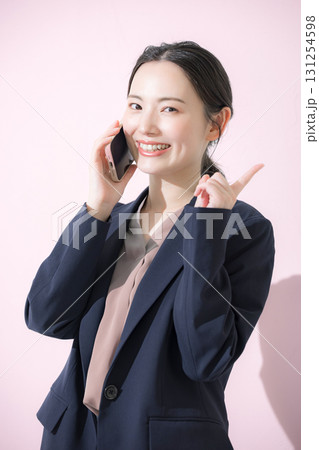 電話をかける通話するスーツを着た若い女性のビジネスシーンの正面の縦　ピンクの背景指差しでオススメ 131254598