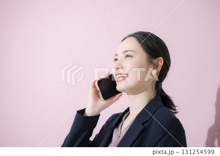 電話をかける通話するスーツを着た若い女性のビジネスシーンの横顔クローズアップ　ピンクの背景	 131254599