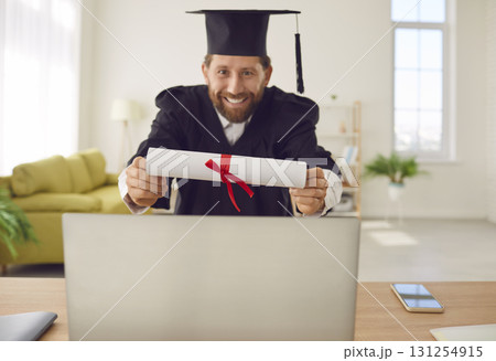 Happy graduate man showing his diploma via laptop having online video call. 131254915