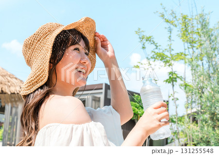 プールサイドでミネラルウォーターを飲む麦わら帽子を被った若い女性 プールサイドでミネラルウォーターを飲む麦わら帽子を被った若い女性 131255548