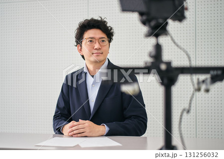 放送スタジオにあるカメラの前で原稿を読んでニュースを伝えるキャスターの男性 131256032