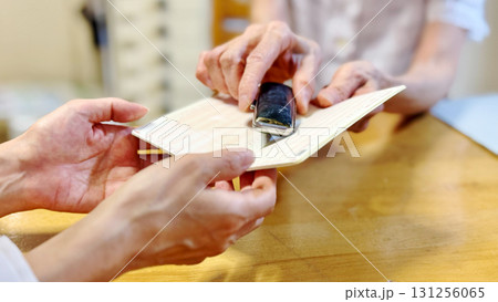 開いた通帳と印鑑ケースを女性に渡す高齢女性の手元_ワイド 131256065