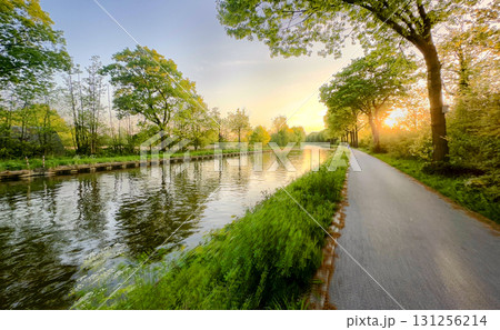 A Beautiful and Serene Canal Pathway Surrounded by Lush Greenary During a Stunning Sunset Glow 131256214