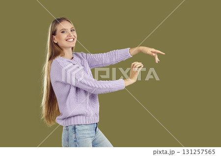 Smiling young woman, dressed in knitted sweater and blue jeans, dances, gracefully stretching her arms in front of her. Smiling young woman, dressed in knitted sweater and blue jeans, dances, gracefully stretching her arms in front of her. 131257565