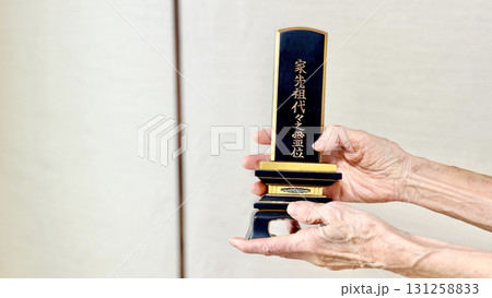 位牌を正面に向けて持つ高齢女性の手元 131258833