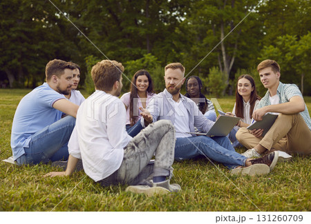 Group of students friends preparing for classes in nature or discussing social media in summer park Group of students friends preparing for classes in nature or discussing social media in summer park 131260709