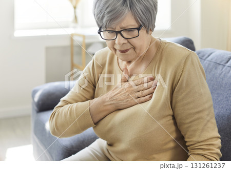 Senior woman sitting alone on sofa in the living room at home suffering from heart attack. 131261237