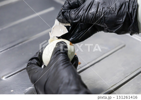 Hygienic hands in black gloves expertly peeling a hard-boiled egg, highlighting careful food preparation and safety standards in a professional kitchen 131261416
