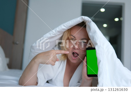 woman applying sheet mask at home in front of double sided mirror.beautiful girl in white robe sitting with coffee or tea cup in hand. relax and wellbeing moment. lot of cosmetic in front of female. woman applying sheet mask at home in front of double sided mirror.beautiful girl in white robe sitting with coffee or tea cup in hand. relax and wellbeing moment. lot of cosmetic in front of female. 131261630