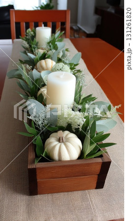 A decorative arrangement with orange and white pumpkins, candles, and autumn leaves creates a warm ambiance for fall gatherings 131261820