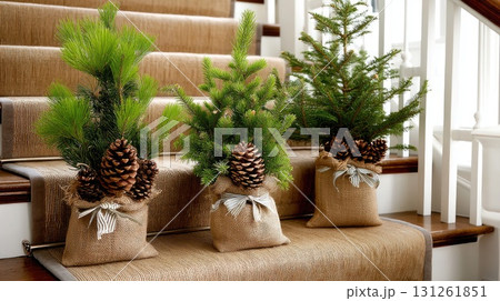 Three small evergreen trees in burlap bags sit on a staircase, adding a festive touch to the home during the holiday season 131261851