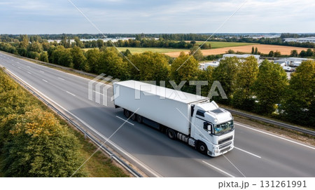 A large white truck travels down a highway surrounded by green fields and rolling hills on a cloudy afternoon 131261991