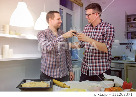 Men gay clink glasses, drink wine and cook pizza in the kitchen. Gay family life. Men gay clink glasses, drink wine and cook pizza in the kitchen. Gay family life. 131262371