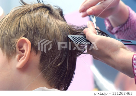 Hairdresser cutting hairs with scissors on boy's head. Back view, stylist's hands close-up. 131262463