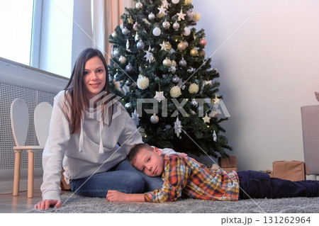 Mom stroking son on back near Christmas tree at home in living room, New Year. 131262964