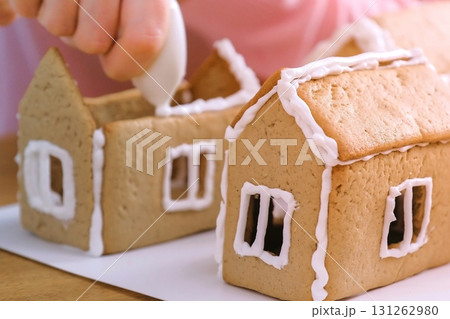 Woman's hands make gingerbread houses glues details with sugar sweet icing. Cooking homemade gingerbread house. Woman's hands make gingerbread houses glues details with sugar sweet icing. Cooking homemade gingerbread house. 131262980
