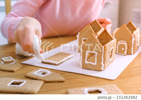 Woman's hands make gingerbread houses glues details with sugar sweet icing. Cooking homemade gingerbread house. Woman's hands make gingerbread houses glues details with sugar sweet icing. Cooking homemade gingerbread house. 131262982