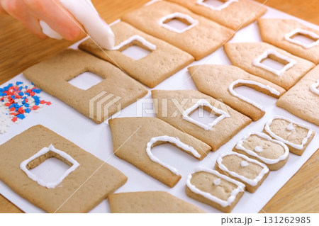 Woman's hands decorate with sugar sweet icing cookies for gingerbread houses. Cooking homemade gingerbread house. 131262985
