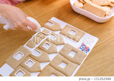 Woman's hands decorate with sugar sweet icing cookies for gingerbread houses. Cooking homemade gingerbread house. Woman's hands decorate with sugar sweet icing cookies for gingerbread houses. Cooking homemade gingerbread house. 131262986
