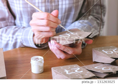 Woman makes christmas advent calendar for kids. Writes a number on the bag by brush and white paint. Close-up hands. Woman makes christmas advent calendar for kids. Writes a number on the bag by brush and white paint. Close-up hands. 131263025