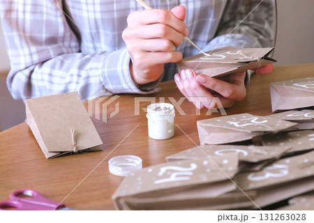 Woman makes christmas advent calendar for kids. Writes a number on the bag by brush and white paint. Close-up hands. Woman makes christmas advent calendar for kids. Writes a number on the bag by brush and white paint. Close-up hands. 131263028