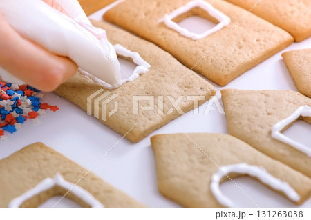 Woman's hands decorate with sugar sweet icing cookies for gingerbread houses. Cooking homemade gingerbread house. Woman's hands decorate with sugar sweet icing cookies for gingerbread houses. Cooking homemade gingerbread house. 131263038