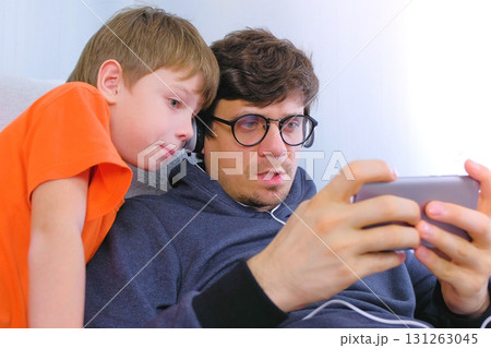 Man in glasses and headphones playing a game in smartphone with his son. Gamer relax. 131263045