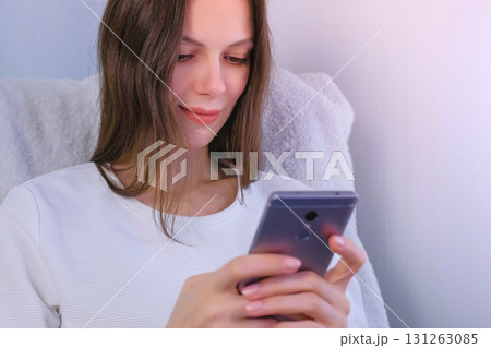 Young brunette woman is reading a book on mobile phone sitting in armchair. Young brunette woman is reading a book on mobile phone sitting in armchair. 131263085