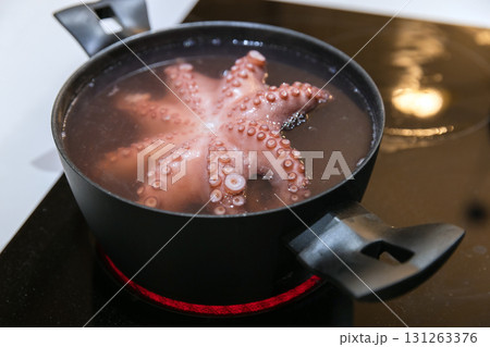 A pink octopus bubbles in simmering water inside a black pot on a glass stove top A pink octopus bubbles in simmering water inside a black pot on a glass stove top 131263376