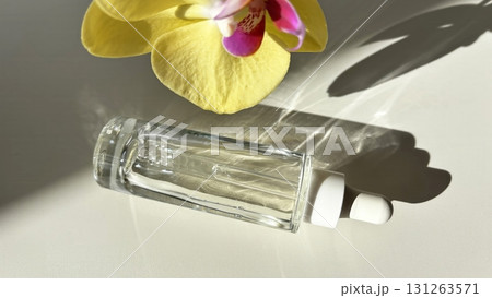 Glass cosmetic dropper with transparent facial serum and bottle on light background with orchid and natural sunlight. Beauty skincare product Glass cosmetic dropper with transparent facial serum and bottle on light background with orchid and natural sunlight. Beauty skincare product 131263571