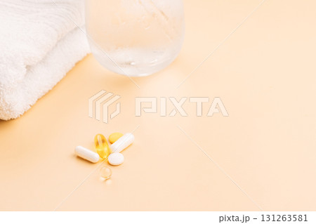 Vitamin pills on beige desktop with towel and dewy glass simple self care scene Vitamin pills on beige desktop with towel and dewy glass simple self care scene 131263581