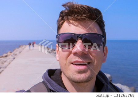 Portrait man video chats selfie smartphone on sea beach pier walks and smiles. Portrait man video chats selfie smartphone on sea beach pier walks and smiles. 131263769