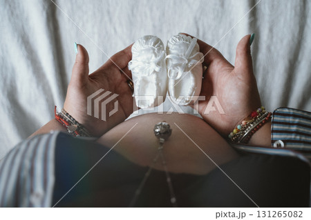 Expectant Mother Holding Baby Shoes Over Belly Expectant Mother Holding Baby Shoes Over Belly 131265082