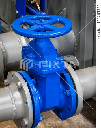 Blue industrial valve installed on a large pipe in a factory setting during daytime Blue industrial valve installed on a large pipe in a factory setting during daytime 131265552