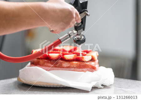 A pastry chef applying icing to a cake with a professional icing gun. The chef hands are clearly 131266013