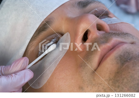 Woman applies solution on man's eyelashes for laminating lifting lash procedure. Woman applies solution on man's eyelashes for laminating lifting lash procedure. 131266082
