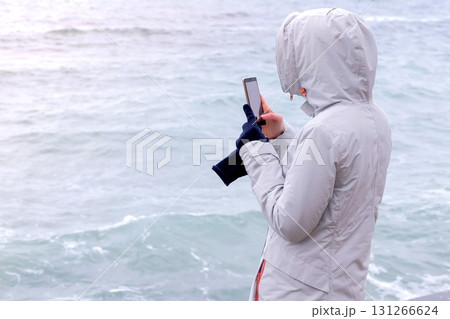 Woman in a white jacket takes a mobile phone big storm waves. Back view. Woman in a white jacket takes a mobile phone big storm waves. Back view. 131266624
