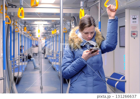 Woman rides in an empty subway car and browsing on her smartphone. Stands and holds the handrail. 131266637
